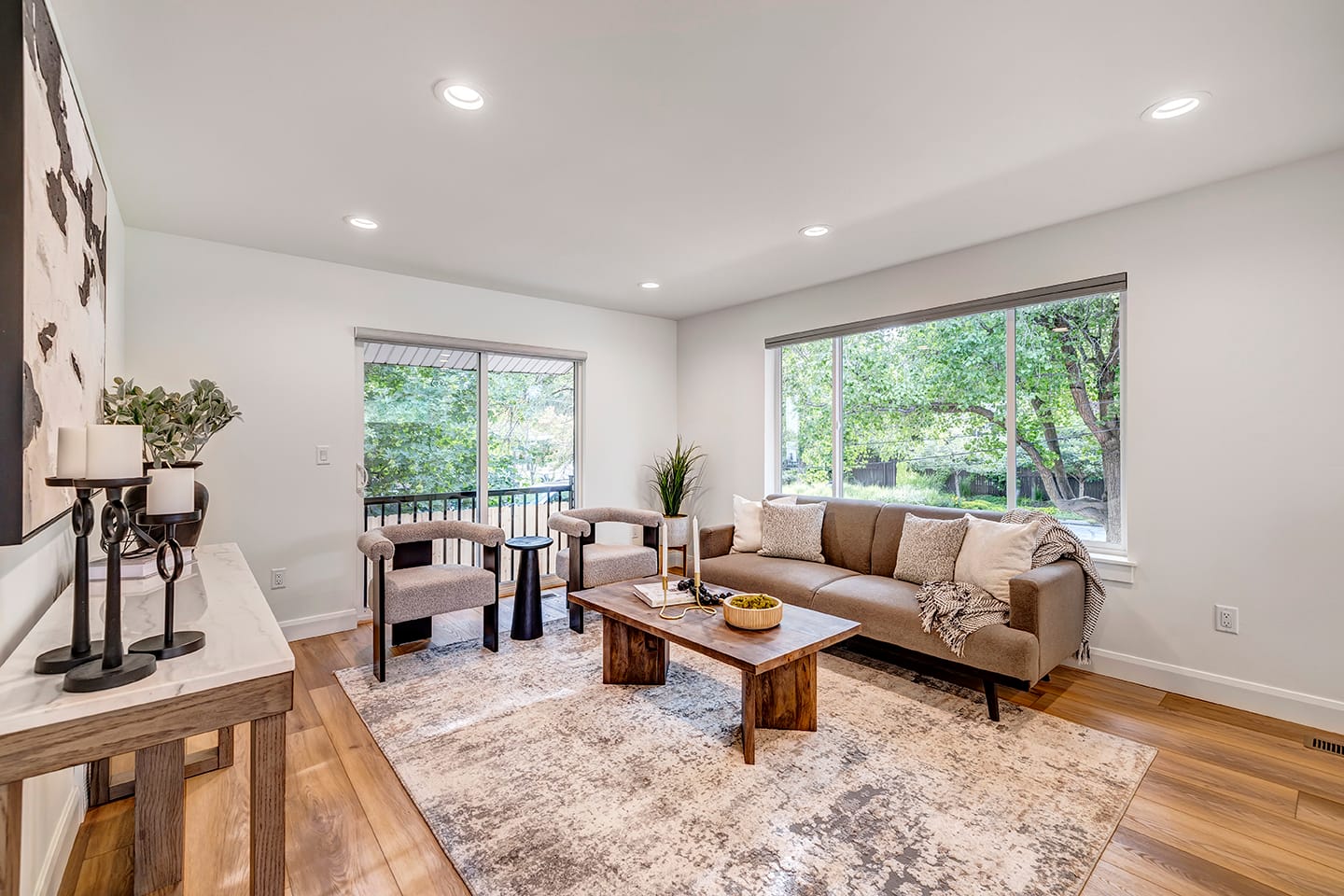 Large living room with a couch, coffee table, and two chairs. The space also includes a large window above the couch and a sliding door behind the two chairs.