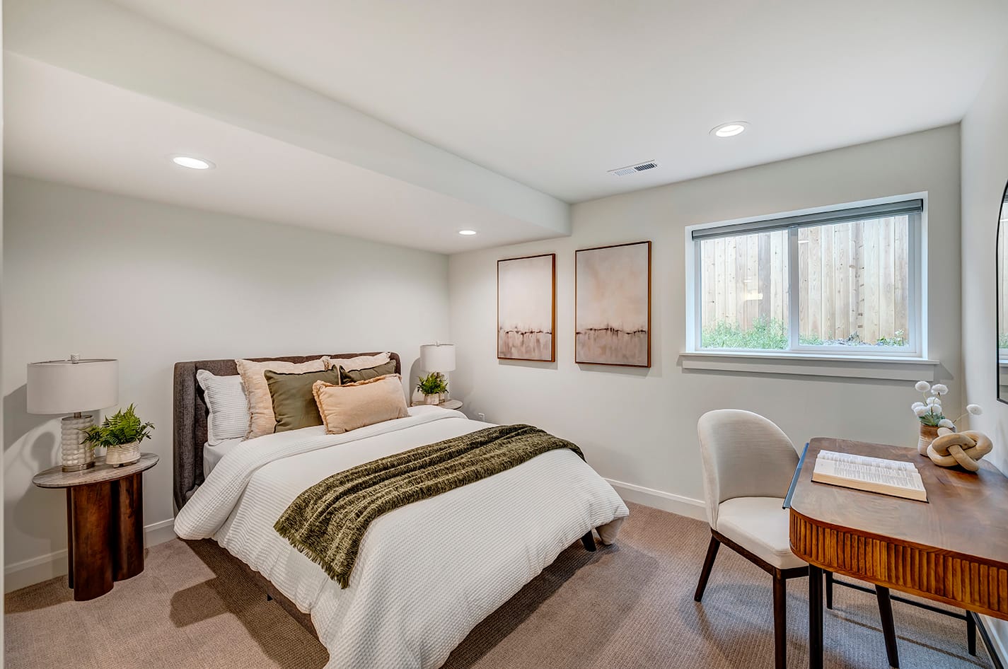Bedroom showing the bed and nightstands on the wall to the left, two pictures and a window on the wall ahead, and a desk on the wall to the right.