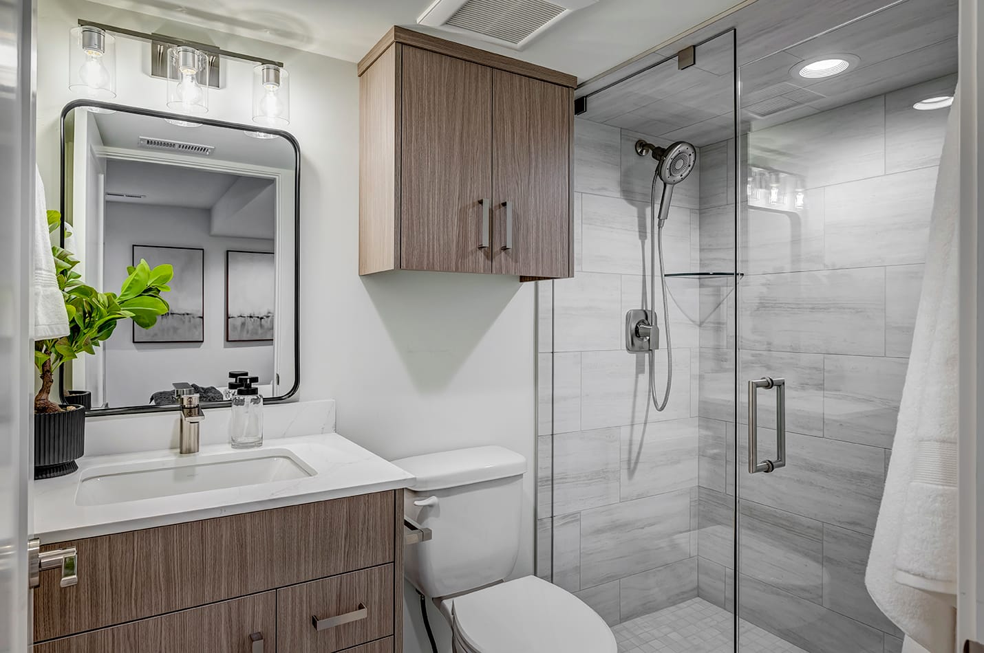 Updated bathroom with a shower, toilet with cabinet above, and a sink.