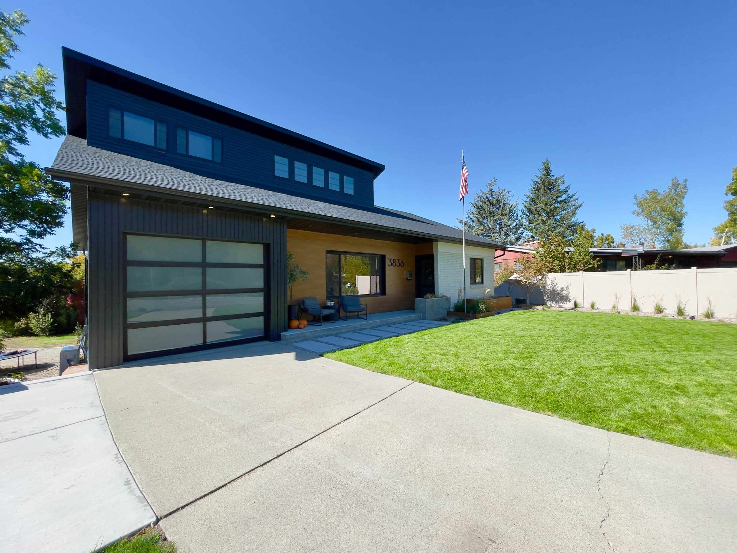 Exterior of house remodel with a covered front porch, green lawn, and driveway with access to the one car garage.