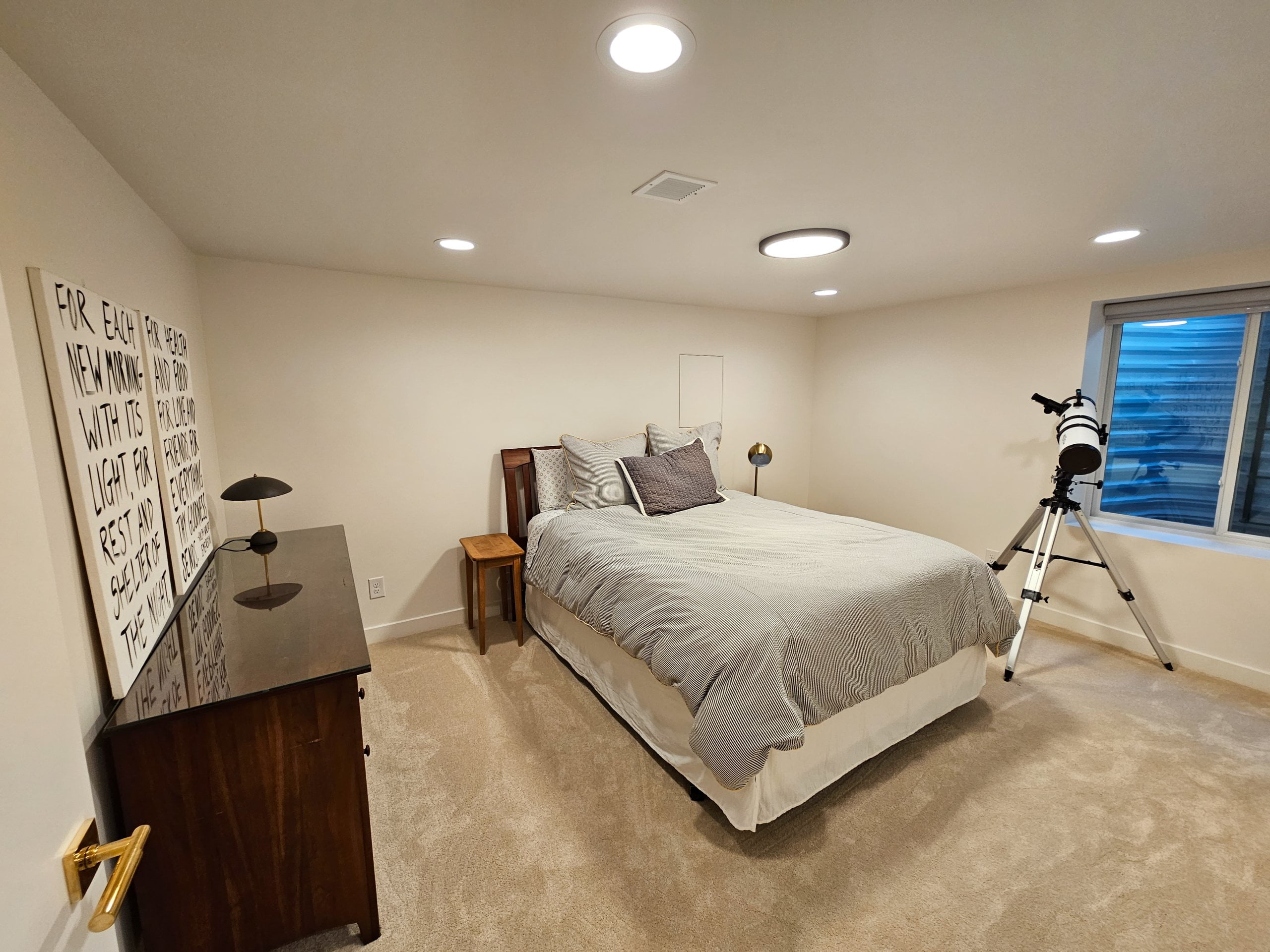 Basement bedroom with an egress window, bed, dresser, and large telescope.