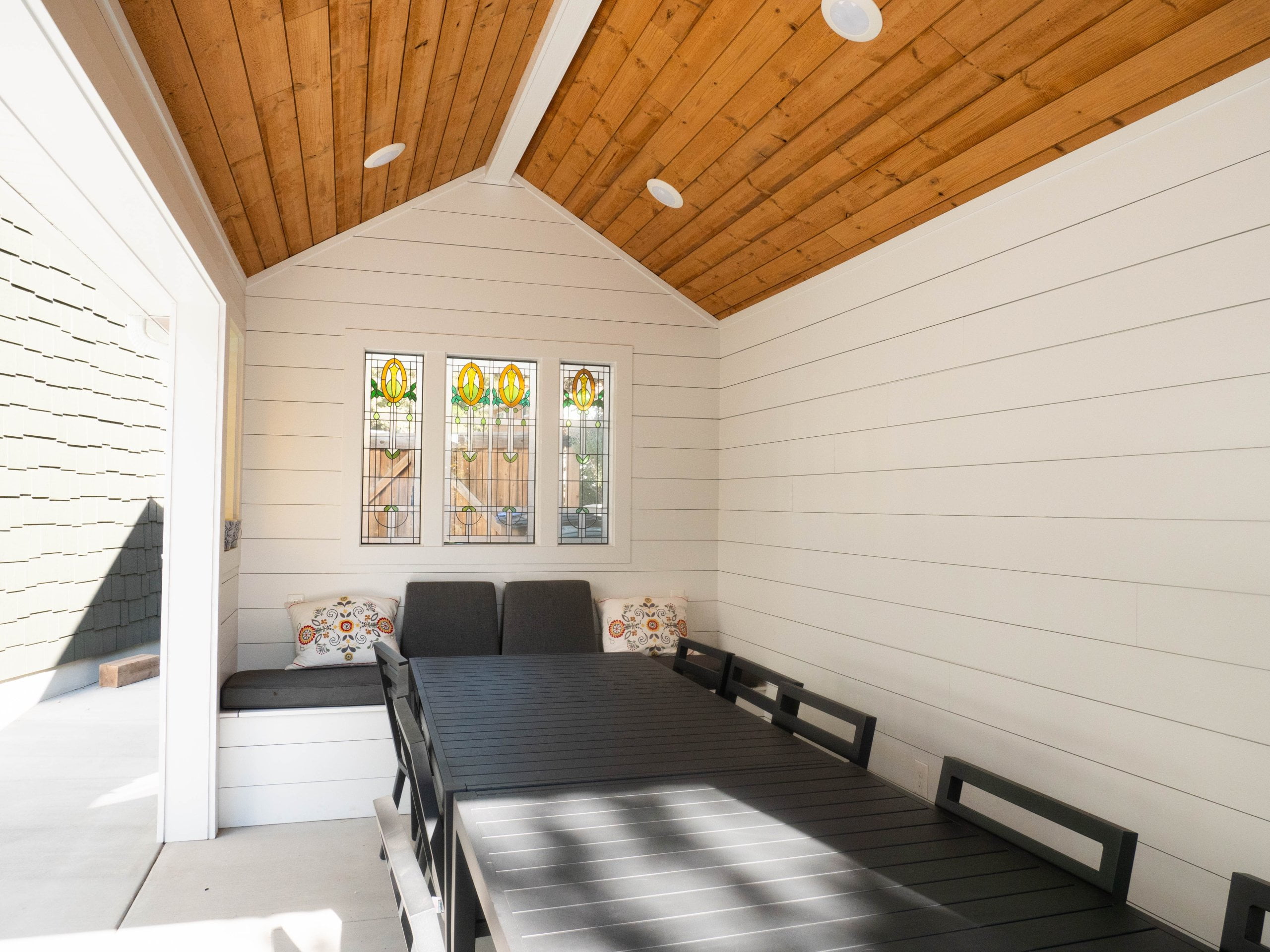 Covered patio with a table and chairs, built-in bench, and stained glass windows.