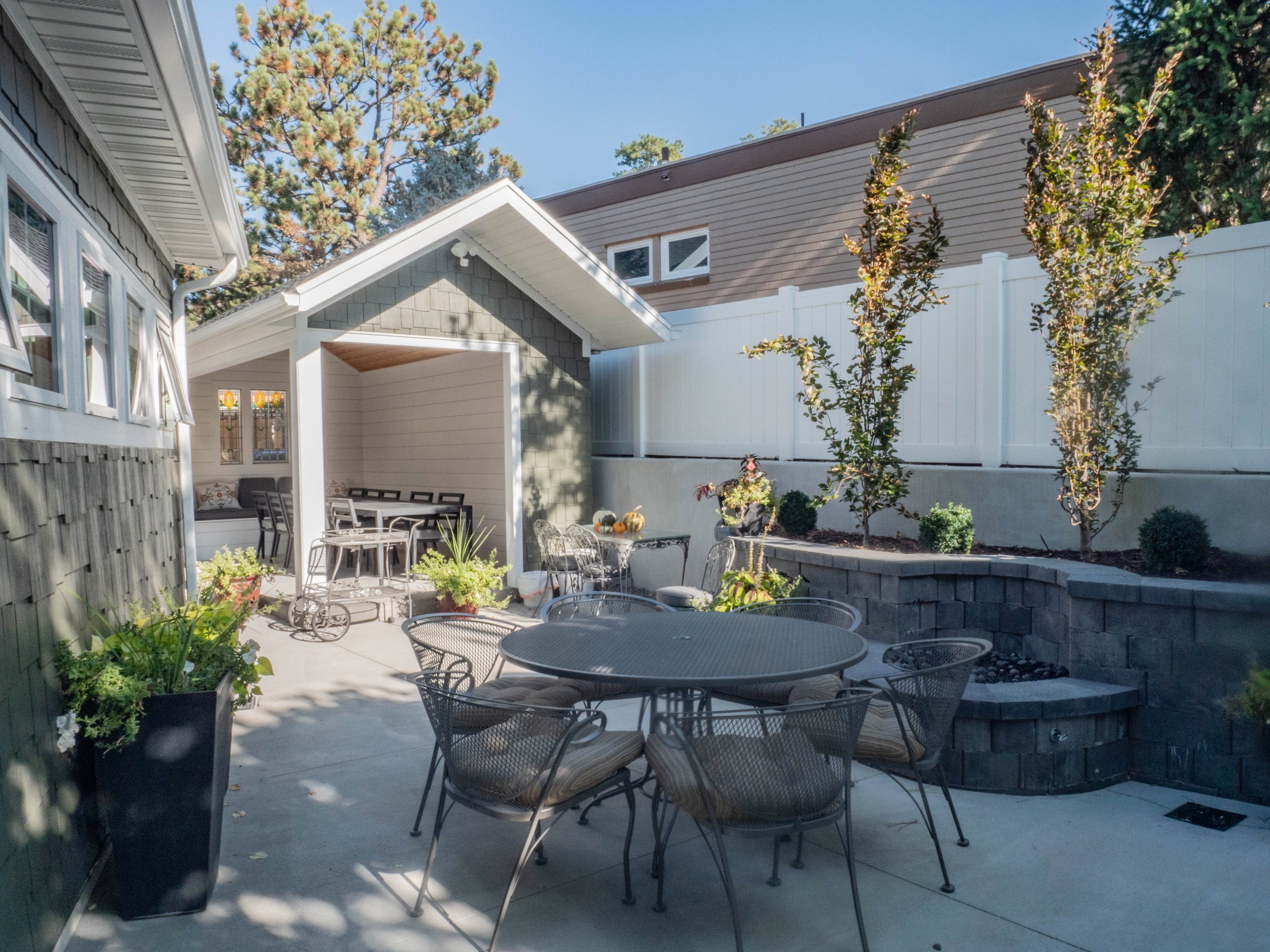 Completed backyard renovation that includes a retaining wall with a firepit, covered patio with seating, and patio area with more seating.