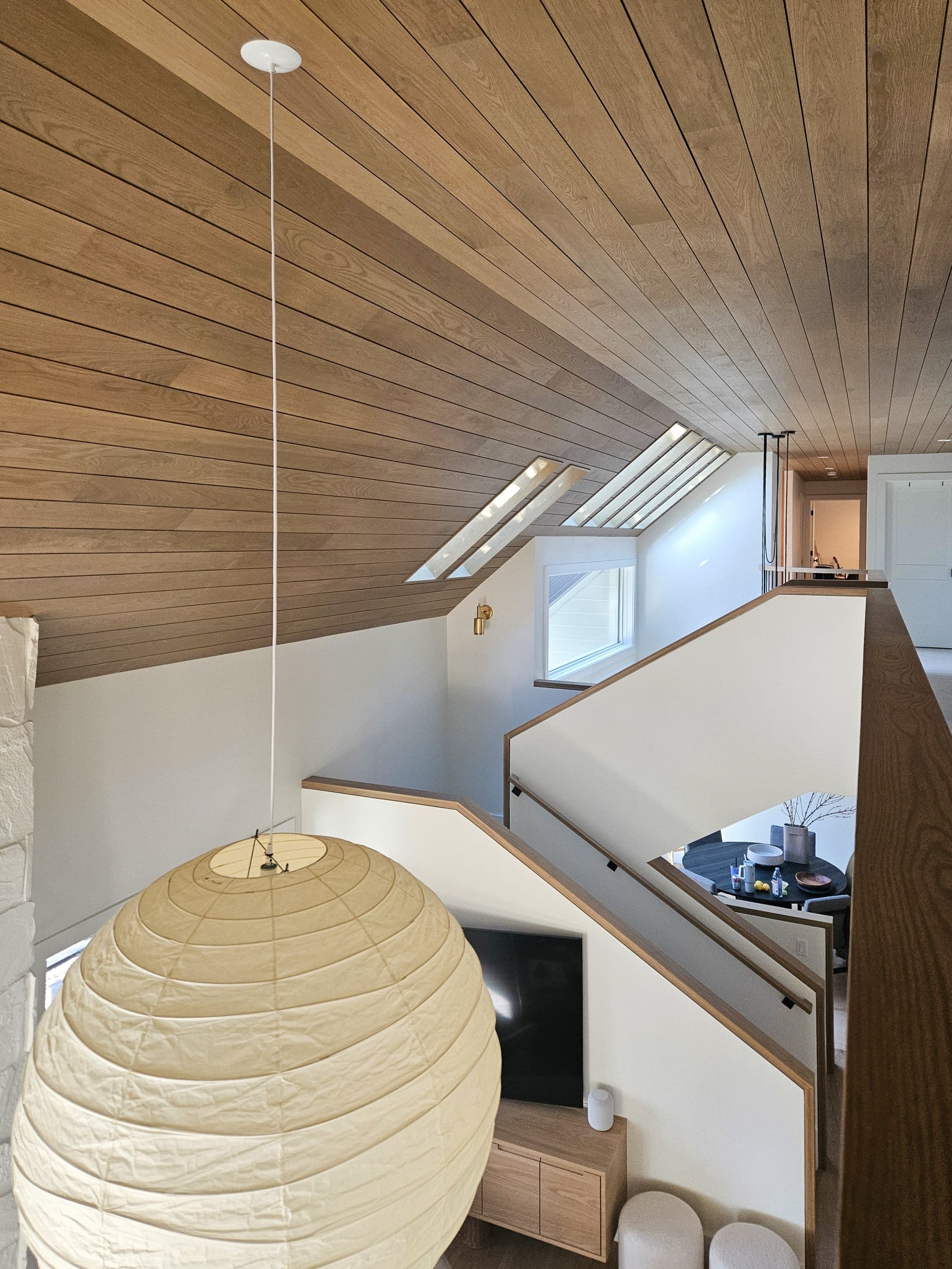View from the second level looking down the hallway towards the stairs with a view over the partial wall to the rooms on the lower level.