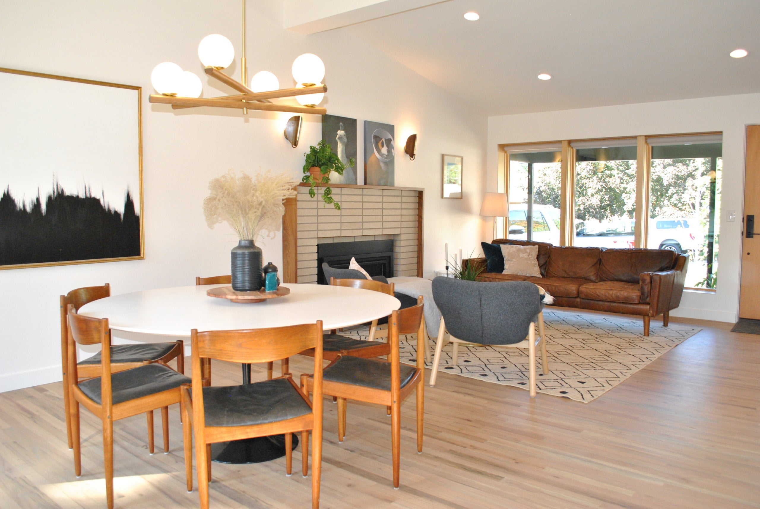 Open concept dining room and living room with vaulted ceilings. The living room includes a couch under the windows, a fireplace, and two chairs, In the dining room is seating for six at a round table.
