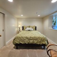 Thumbnail of http://Large%20basement%20guest%20bedroom%20with%20a%20bed,%20small%20side%20table,%20and%20a%20plant%20in%20the%20windowsill.