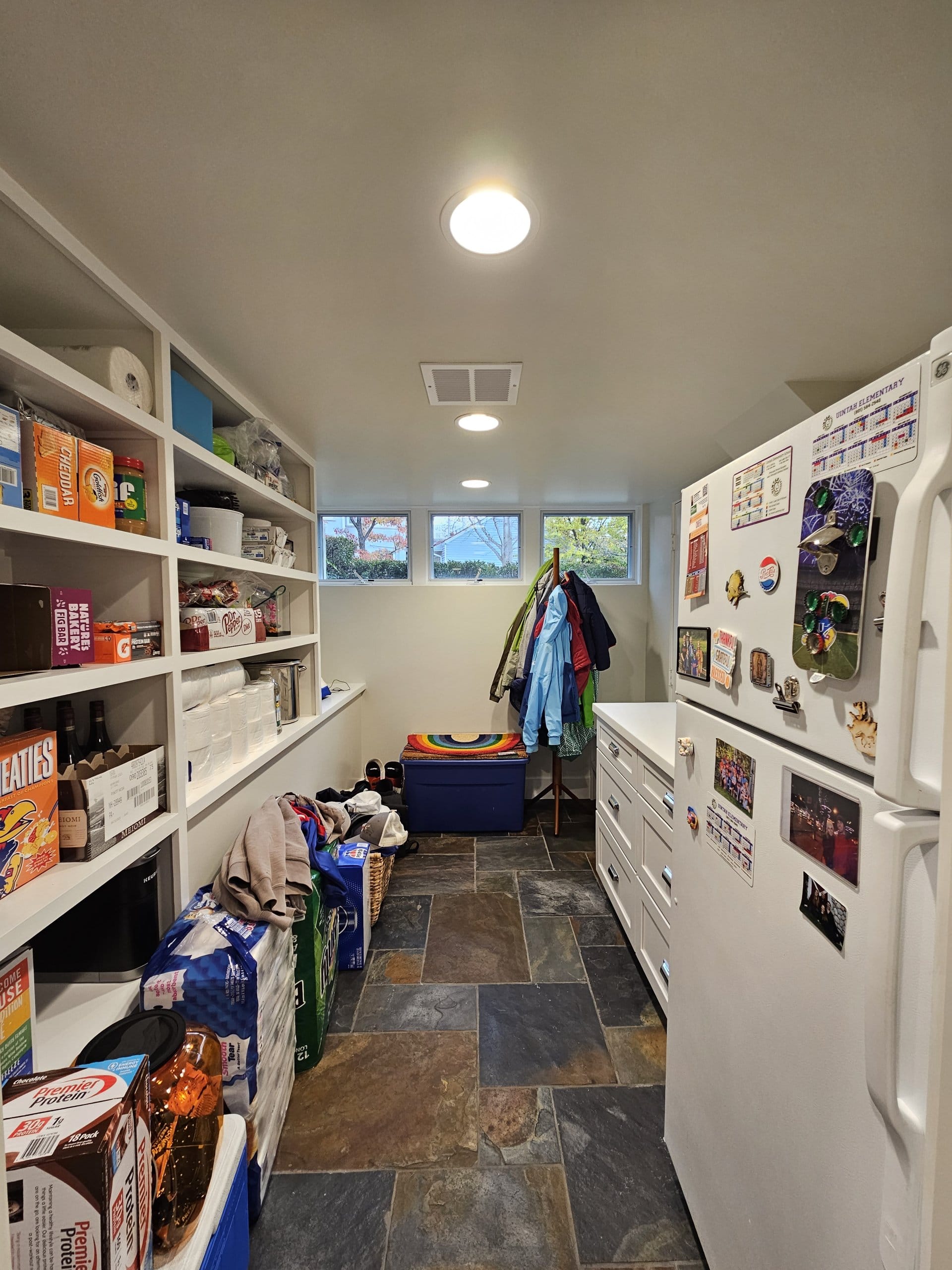 Basement pantry with built-in open shelves, a fridge, and three small windows.