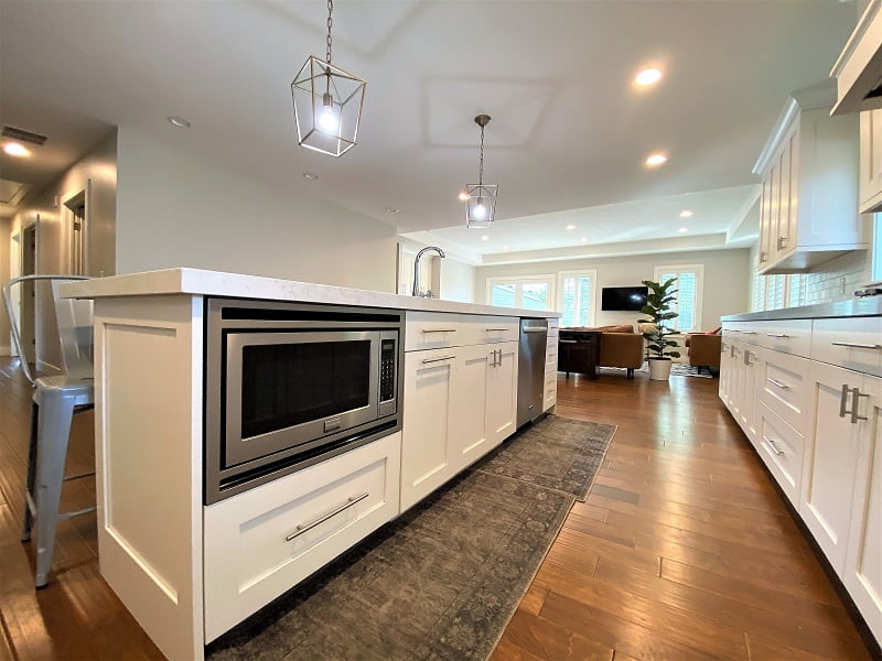 Large kitchen island with microwave, sink, and dishwasher. On the floor in front are two area rugs.