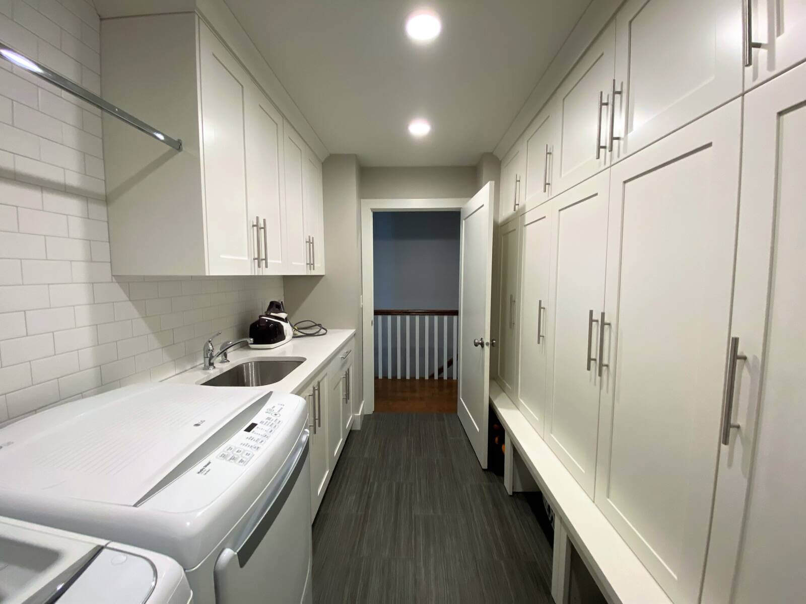 Laundry and mudroom combination with built-in cabinets, a sink, side-by-side washer and dryer, and a door that leads to the hallway.