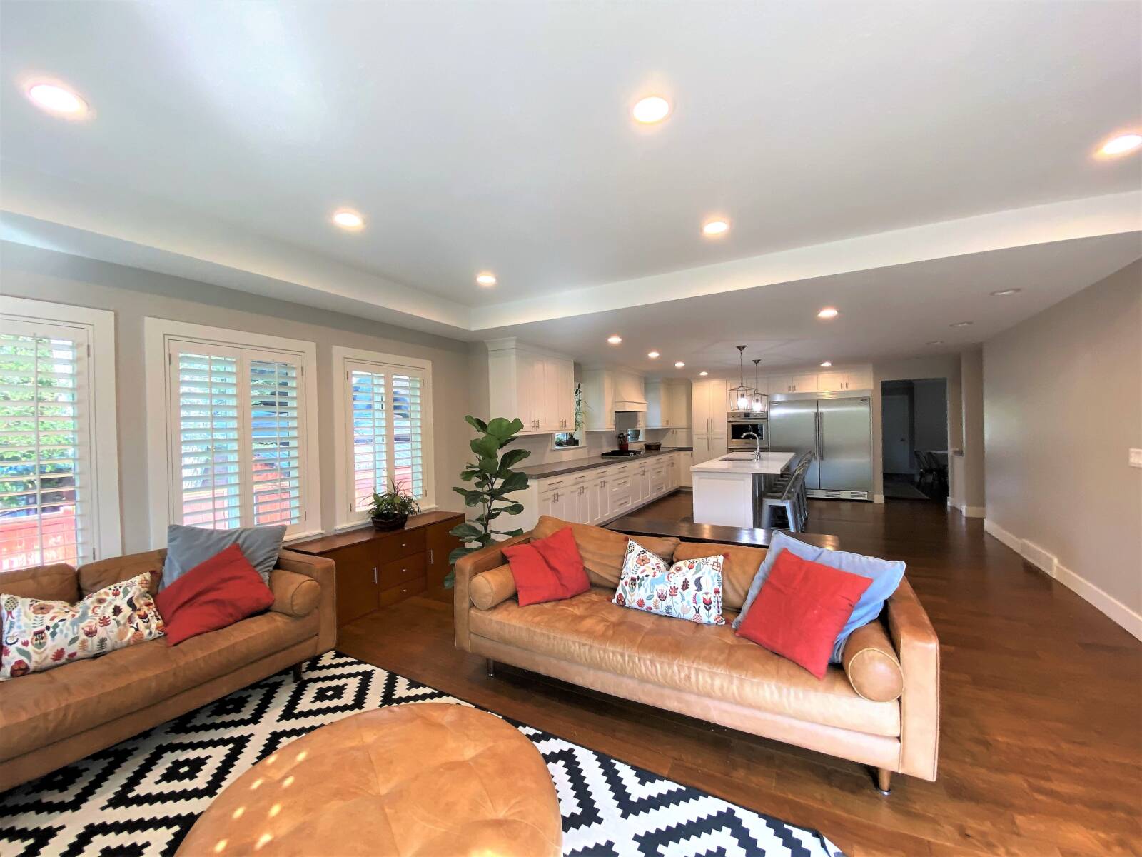 Living room with an open concept layout to the kitchen. The living room includes two couches, a rug, an ottoman, plants, and a credenza.