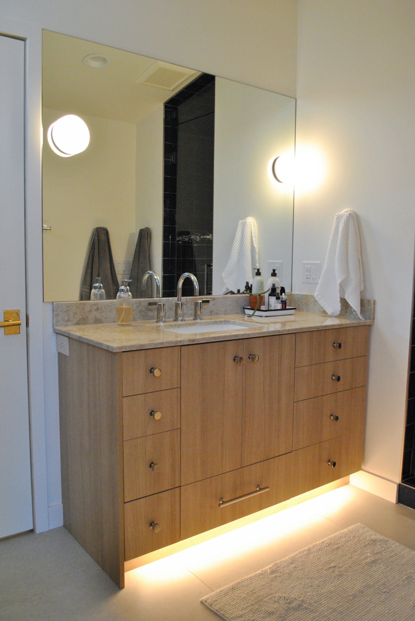 Bathroom vanity sink with light underneath and on the sides of the mirror.