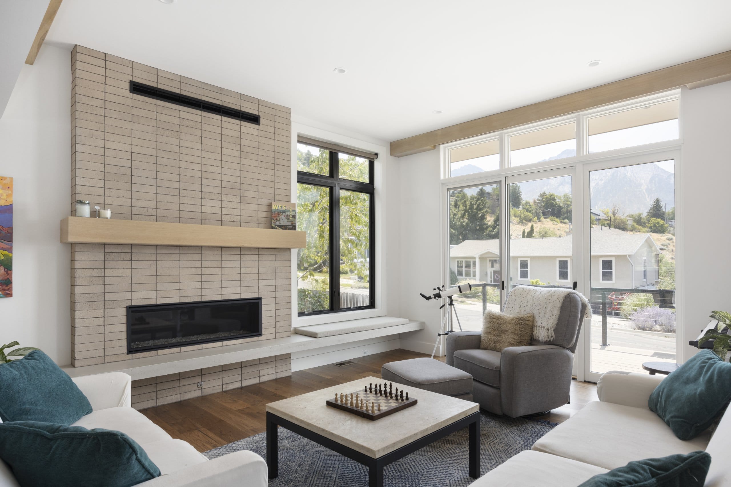 Modern living room that features a door to the balcony and a fireplace with a long bench seat in front of a window.