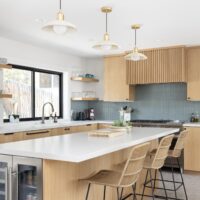 Thumbnail of http://Updated%20modern%20and%20colorful%20kitchen%20with%20the%20sink%20placed%20under%20the%20large%20window,%20wood%20cabinetry,%20terrazzo%20tile%20floors,%20and%20an%20island%20in%20the%20center.