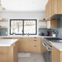 Thumbnail of http://Updated%20modern%20and%20colorful%20kitchen%20with%20the%20sink%20placed%20under%20the%20large%20window,%20wood%20cabinetry,%20terrazzo%20tile%20floors,%20and%20an%20island%20in%20the%20center.