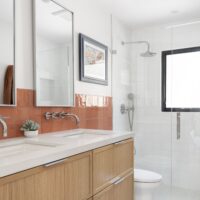 Thumbnail of http://Modern%20bathroom%20with%20double%20sinks,%20toilet,%20and%20a%20window%20in%20the%20shower.%20The%20tile%20is%20neutral%20on%20the%20floor%20and%20in%20the%20shower%20with%20a%20fun%20pop%20of%20orange%20tile%20behind%20the%20vanity.
