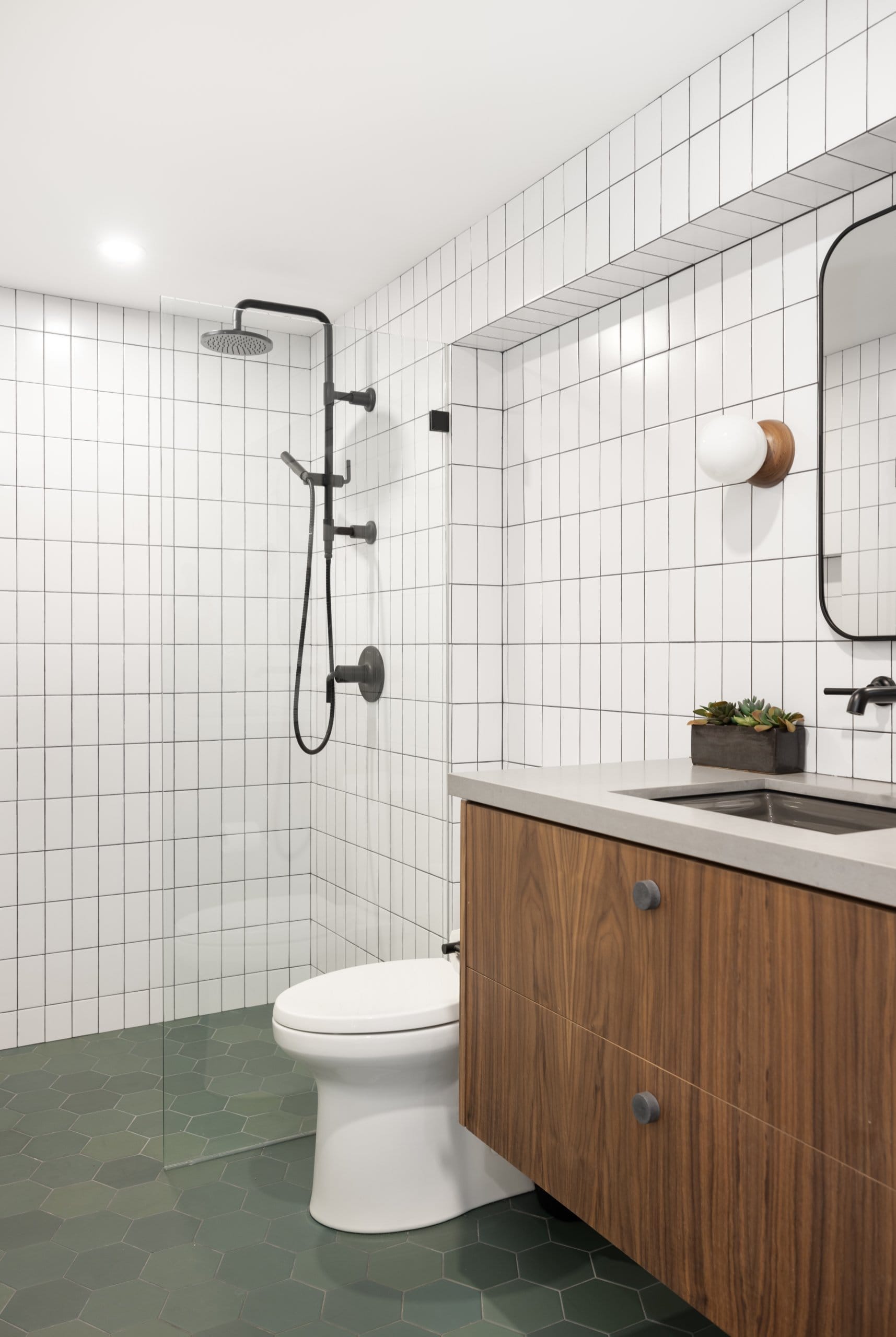 Modern bathroom featuring a curbless shower, wood vanity with storage, and green tiles on the floor and white tiles on the wall.