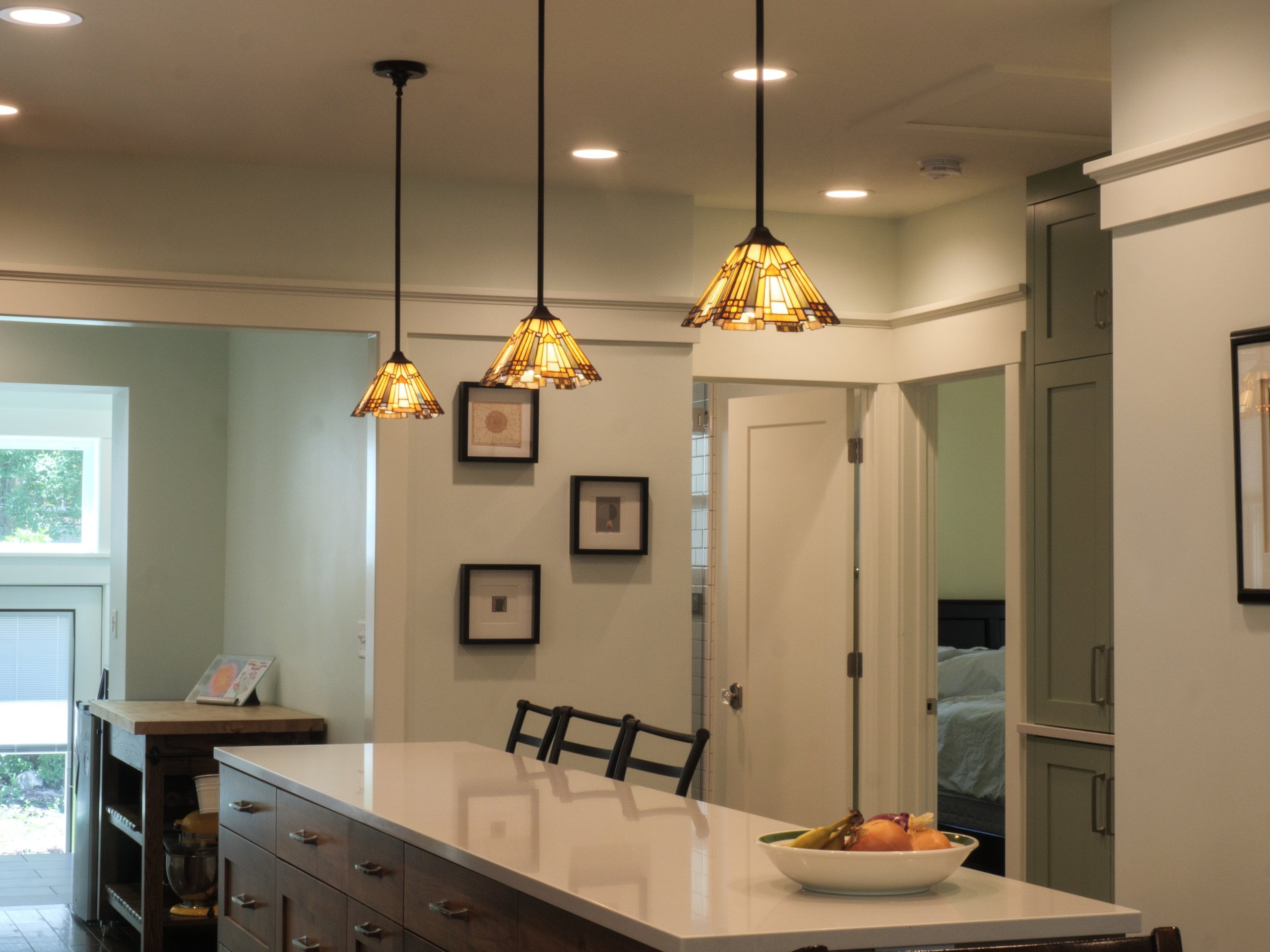 Long kitchen island with seating, storage, and a bowl of fruit on the counter.