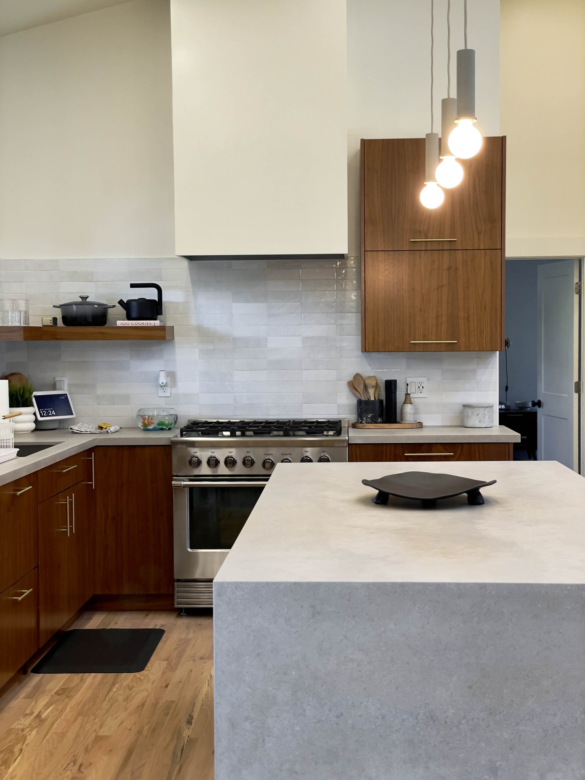 Kitchen with an island in the center, wood cabinetry, tile backsplash, and a range hood above the stove that extends from the wall.
