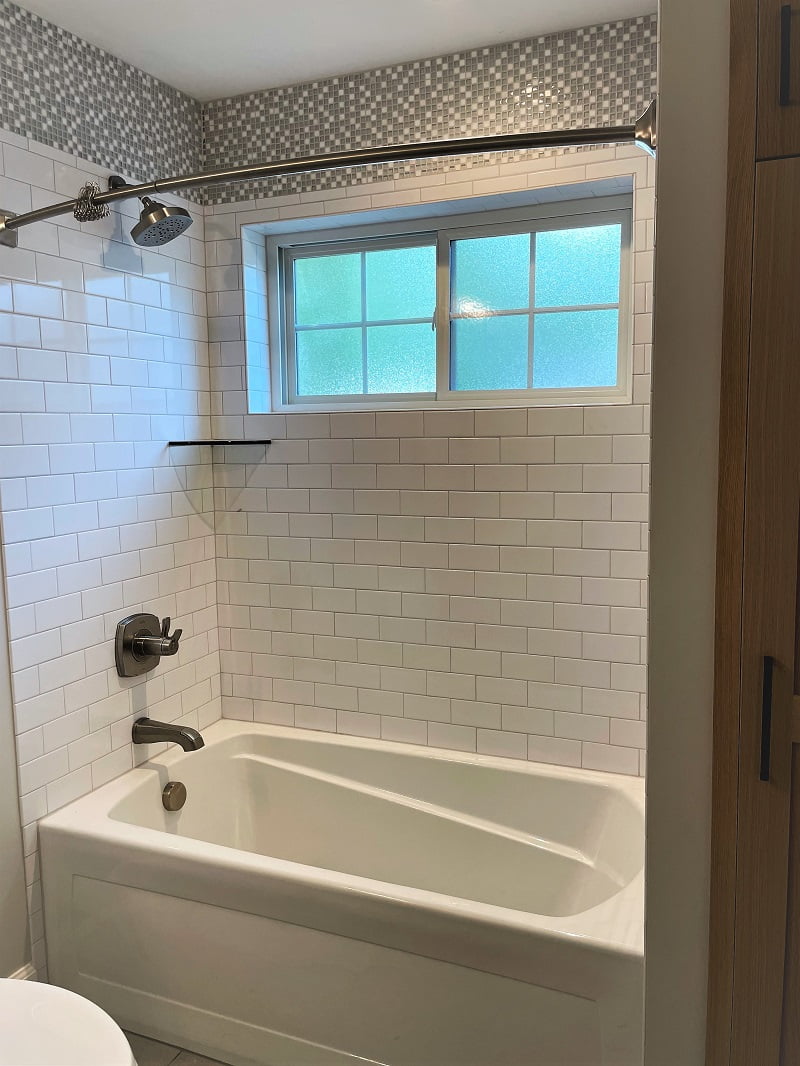 Bath tub and shower combination with a frosted window, shelf, and unique tile design.