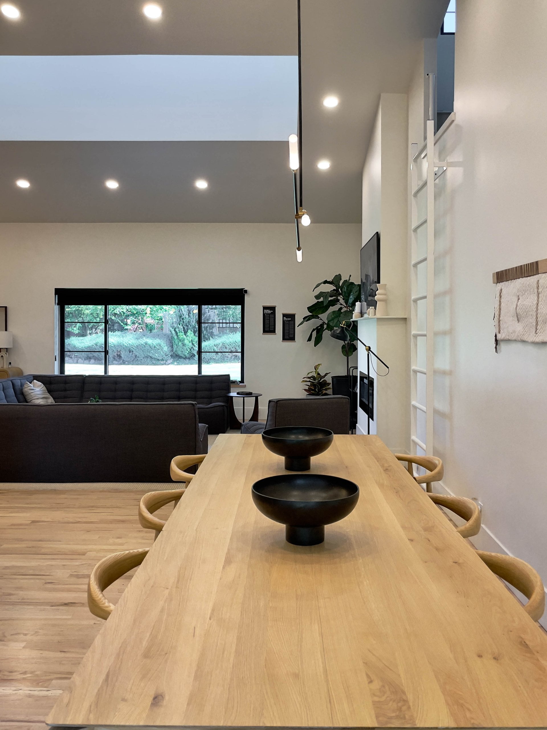 Large open concept dining room with chairs on the long sides and two bowls placed in the center. Beyond the table is a view into the living room and a ladder with access to a loft.