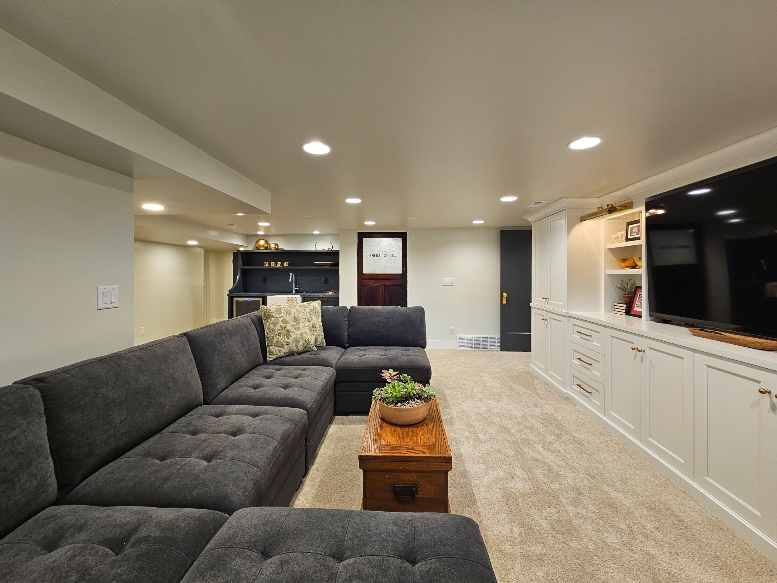 Large basement family room with a couch and coffee table in the center and custom built-ins.