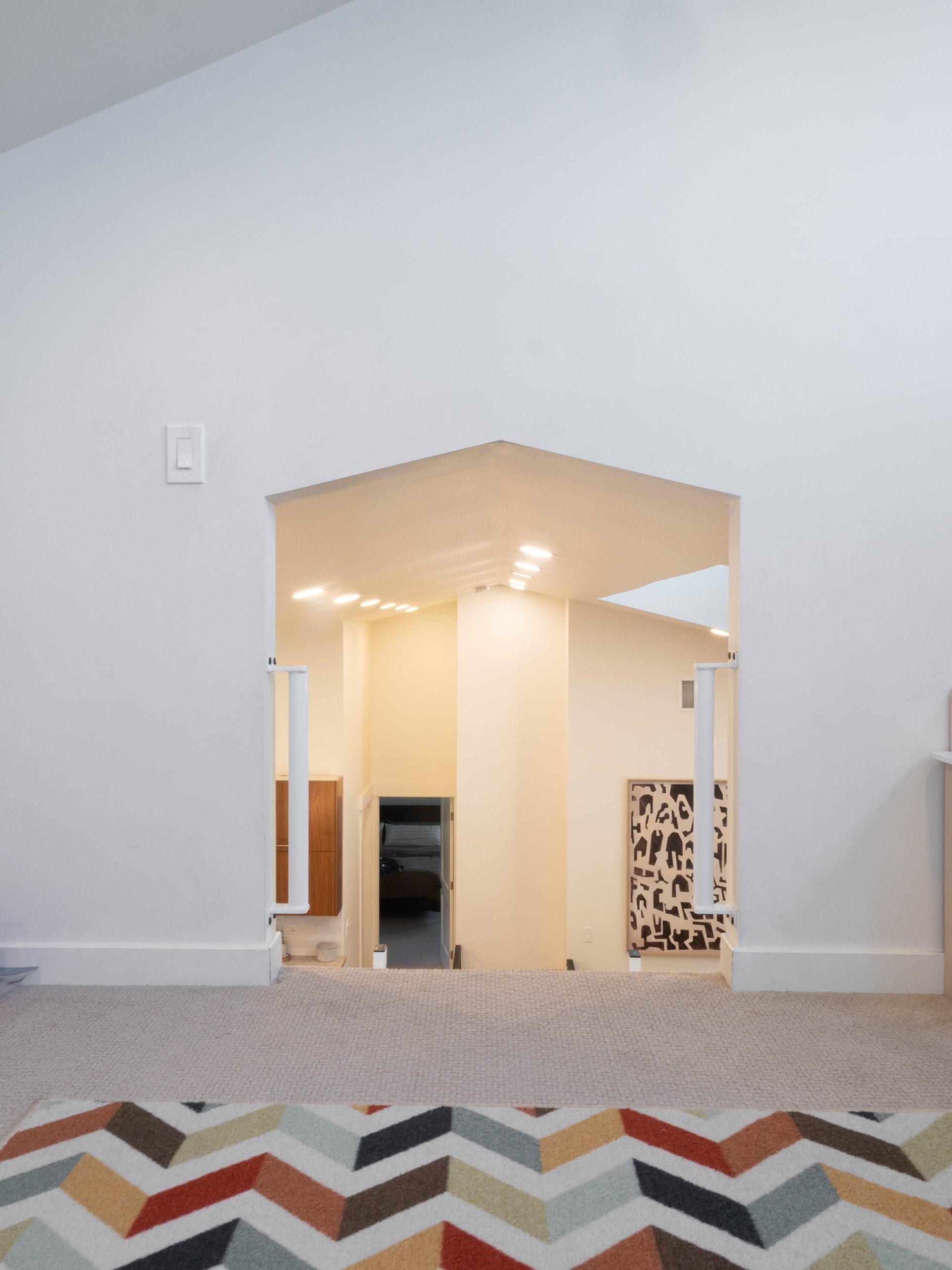Loft with a colorful rug on top of the carpet looking through the opening to the vaulted ceiling in the great room.