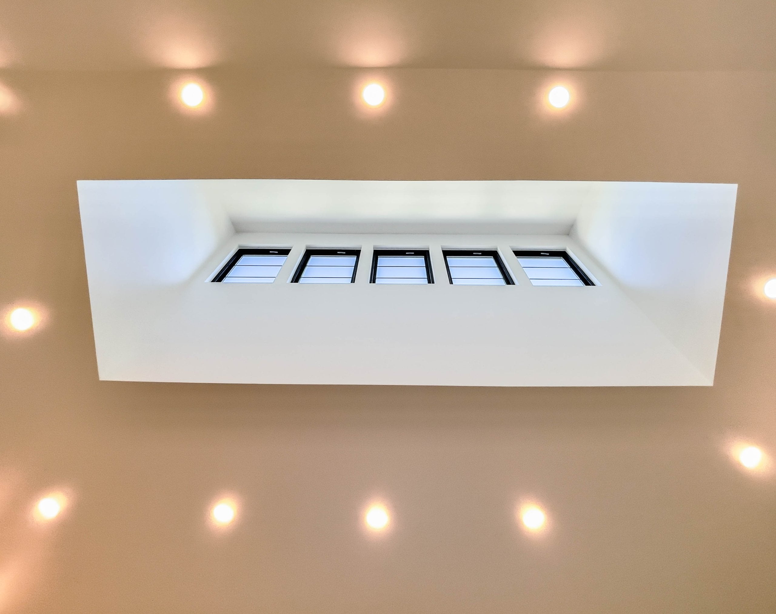 Tall ceiling with the center part extending higher than the perimeter. The center part has five windows while the lower part has canned lights.