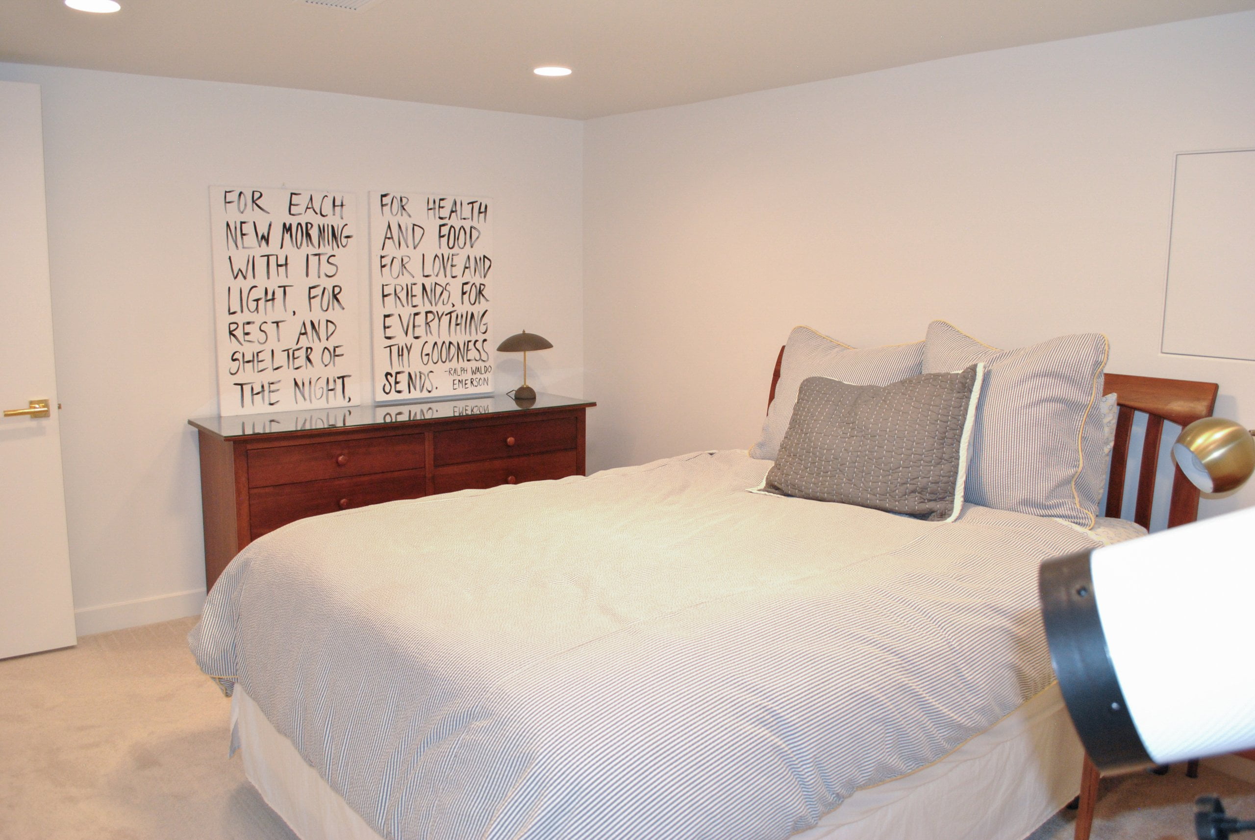 Bedroom with a large bed and dresser. Above the dresser, two pictures with text are hung.