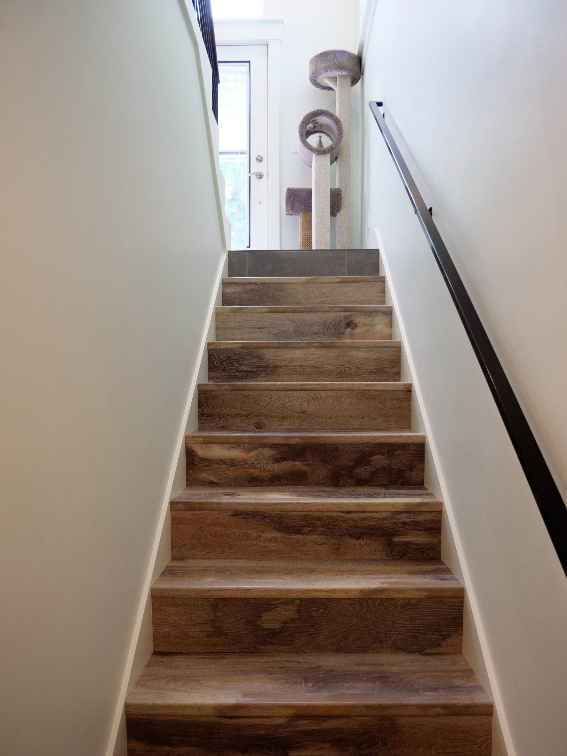 Staircase with a railing and a cat tree at the top next to the door.