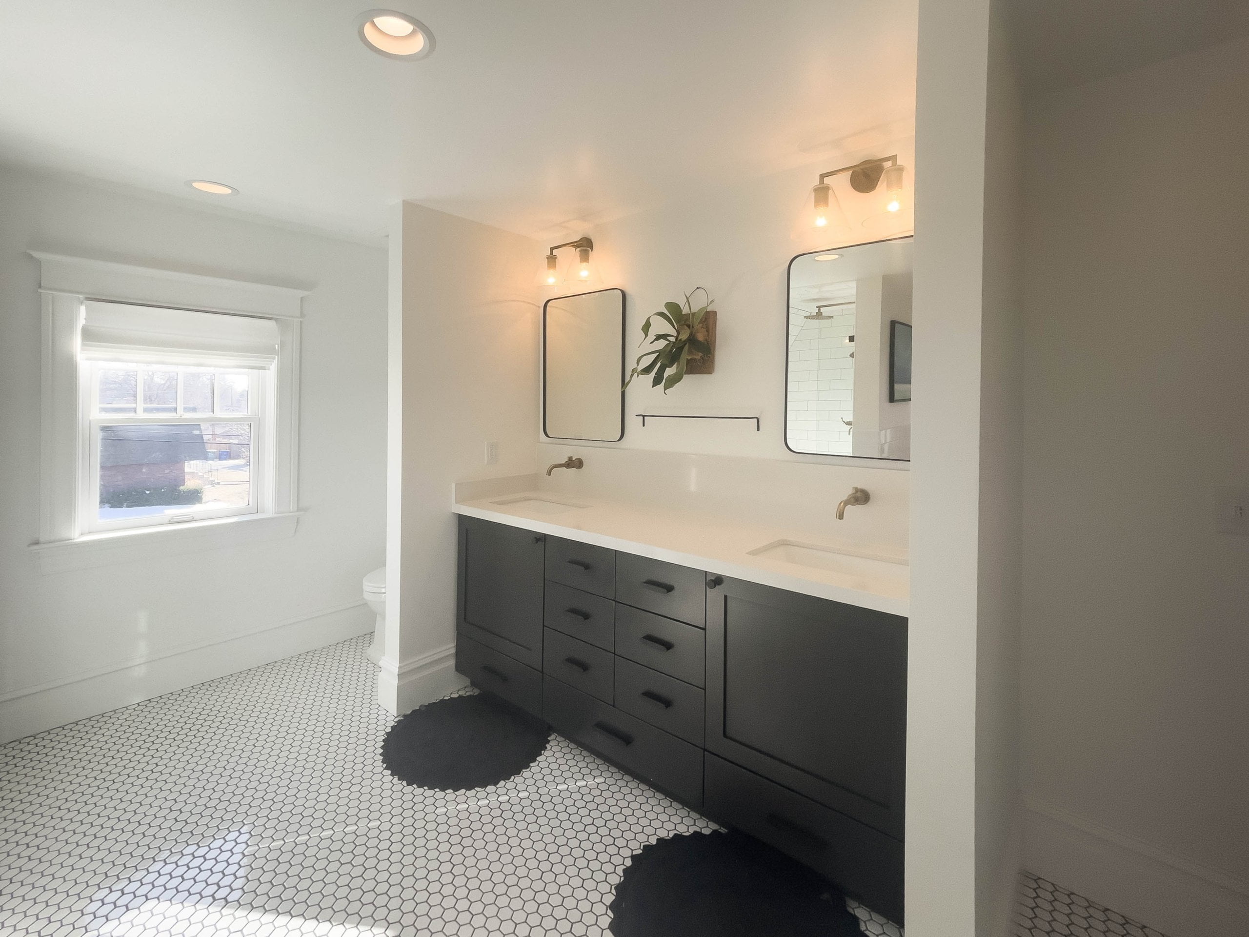 Large primary bathroom with two sinks. Each sink has a round rug on the ground in front of it and a mirror and light fixture above.