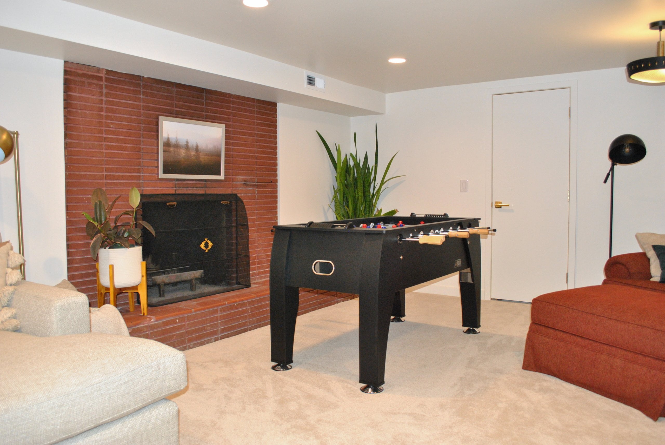 Basement family room with a foosball table in front of a brick fireplace.