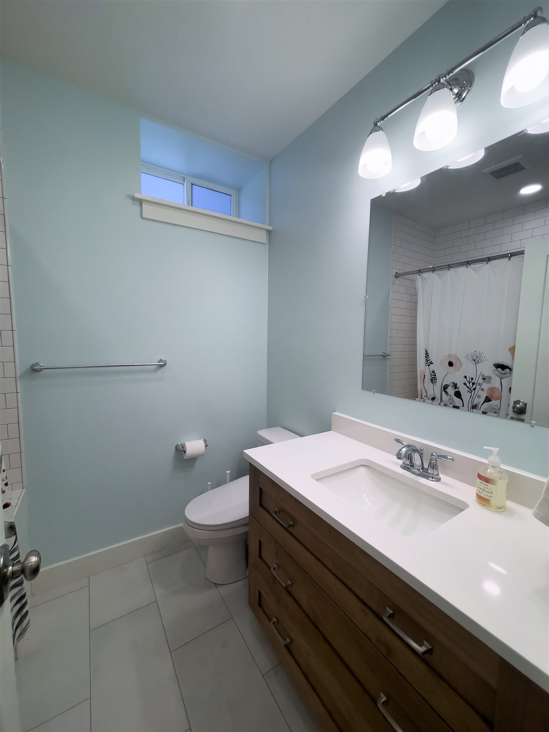 Bathroom with sink and toilet on one wall and the reflection of the shower curtain shown in the mirror above the sink.