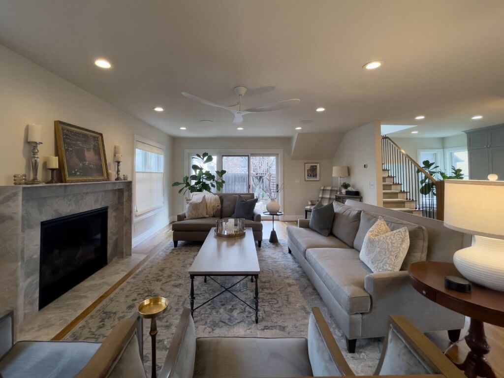 Large family room addition. On the left is a modern fireplace, straight ahead past the furniture are doors to the backyard, and on the right is a staircase and the mudroom.