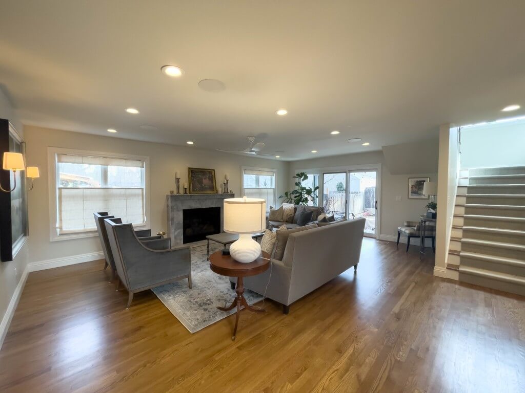 Large family room addition with furniture, windows, and a modern fireplace. On the right is the staircase and doors to the backyard.