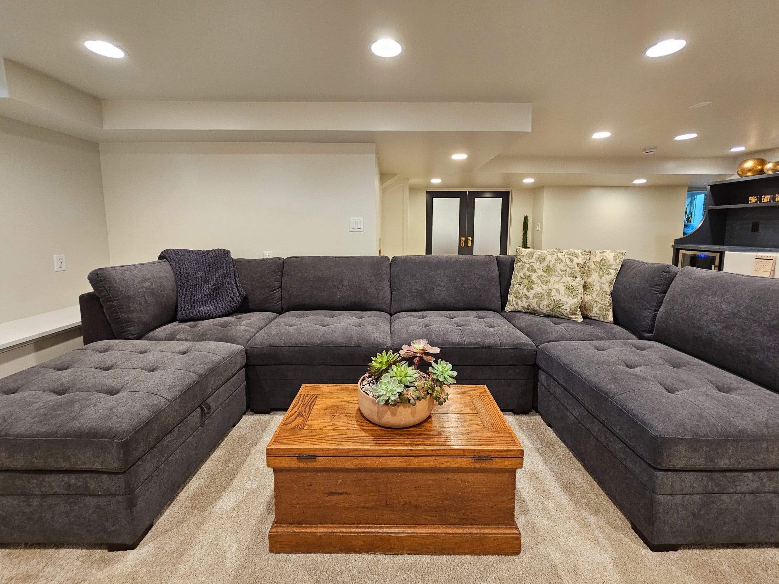 Large basement family room couch with a coffee table in the center and french doors to the craft room behind.