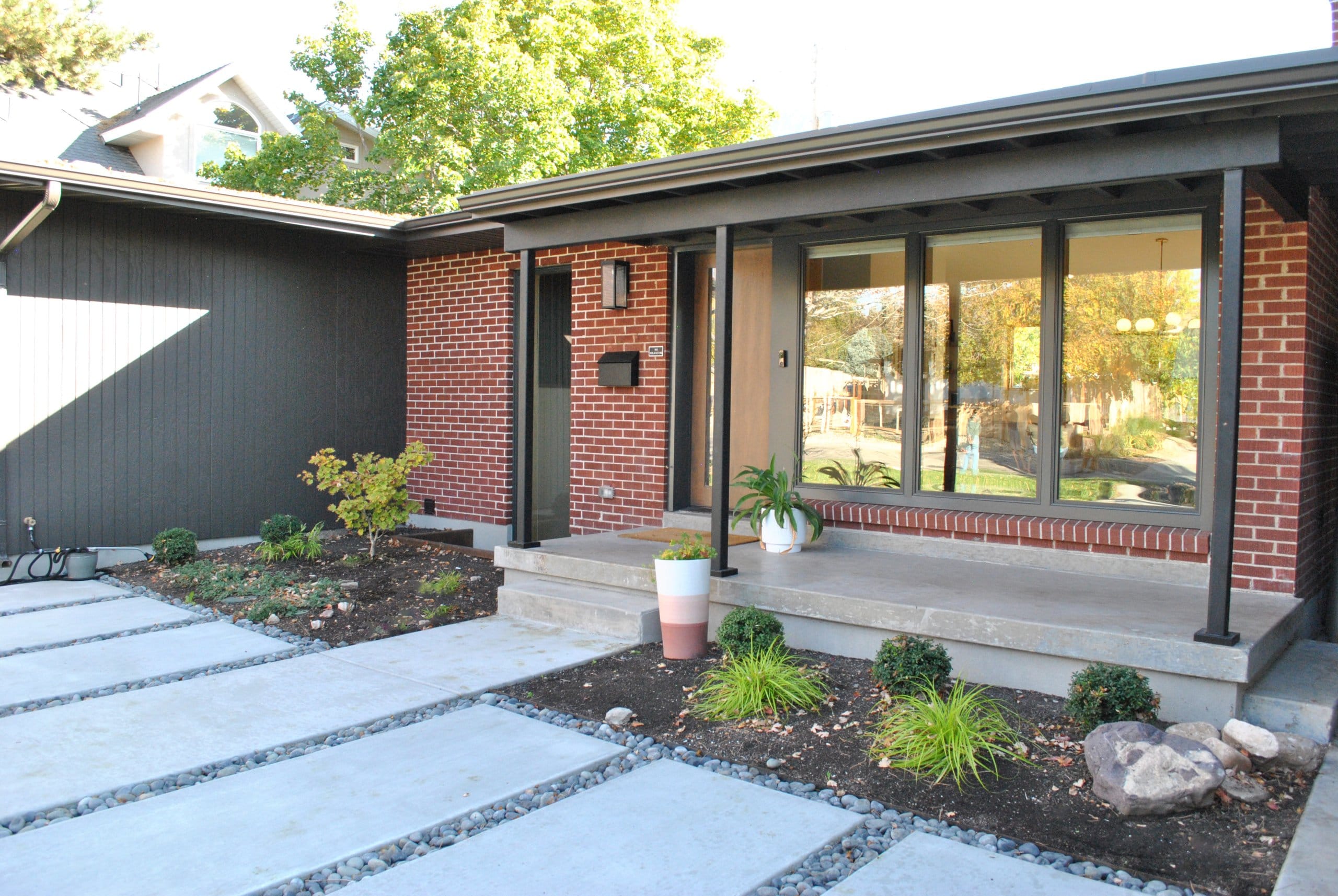 Mid-century modern house exterior with a covered front porch, new landscaping, and large windows.