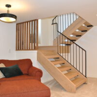 Thumbnail of http://Mid-century%20modern%20staircase%20in%20the%20basement%20family%20room.%20To%20the%20side%20of%20the%20stairs%20is%20a%20large%20orange%20chair%20and%20ottoman.