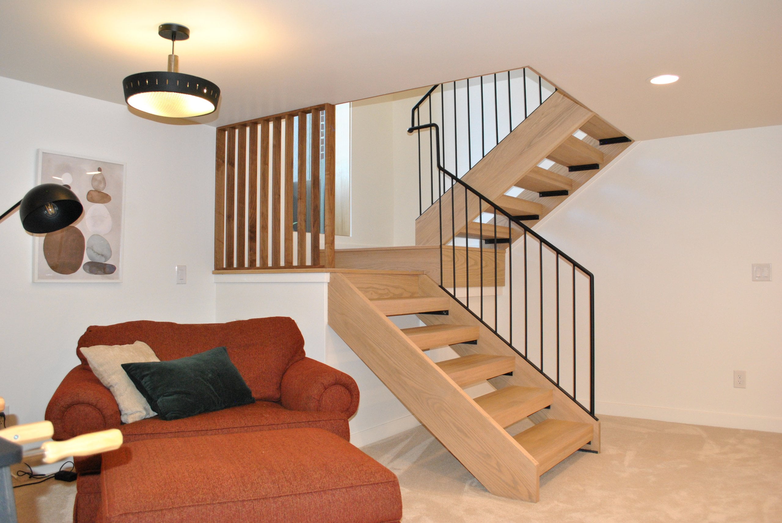 Mid-century modern staircase in the basement family room. To the side of the stairs is a large orange chair and ottoman.