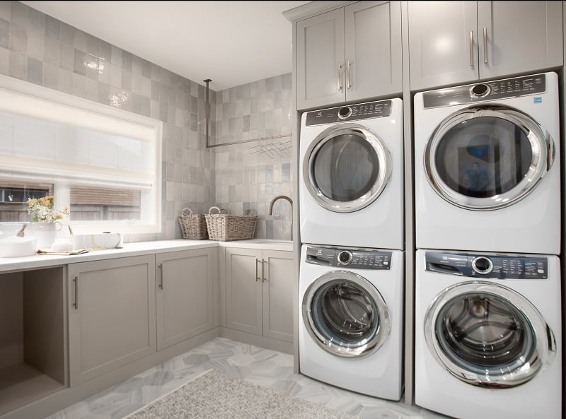 Large, modern laundry room with storage, hanging space, a sink, and two sets of stacked washer and dryers.
