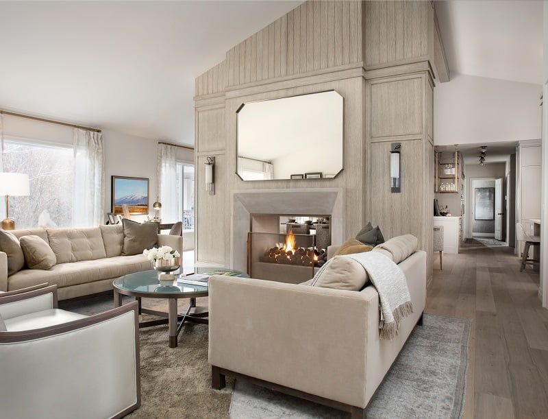 Large fireplace in the living room with openings on either side. The room is furnished with two couches, chairs, a rug, and a coffee table.