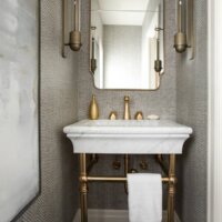 Thumbnail of http://Vanity%20in%20the%20powder%20bathroom%20with%20gold%20fixtures,%20wallpaper,%20and%20a%20hand%20towel%20hung%20under%20the%20open%20sink.