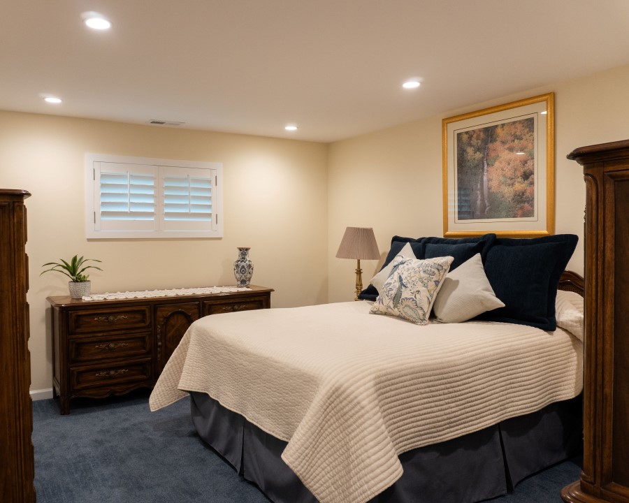 Bedroom with blue carpet, a large bed with a picture above, and a wood dresser with a window above