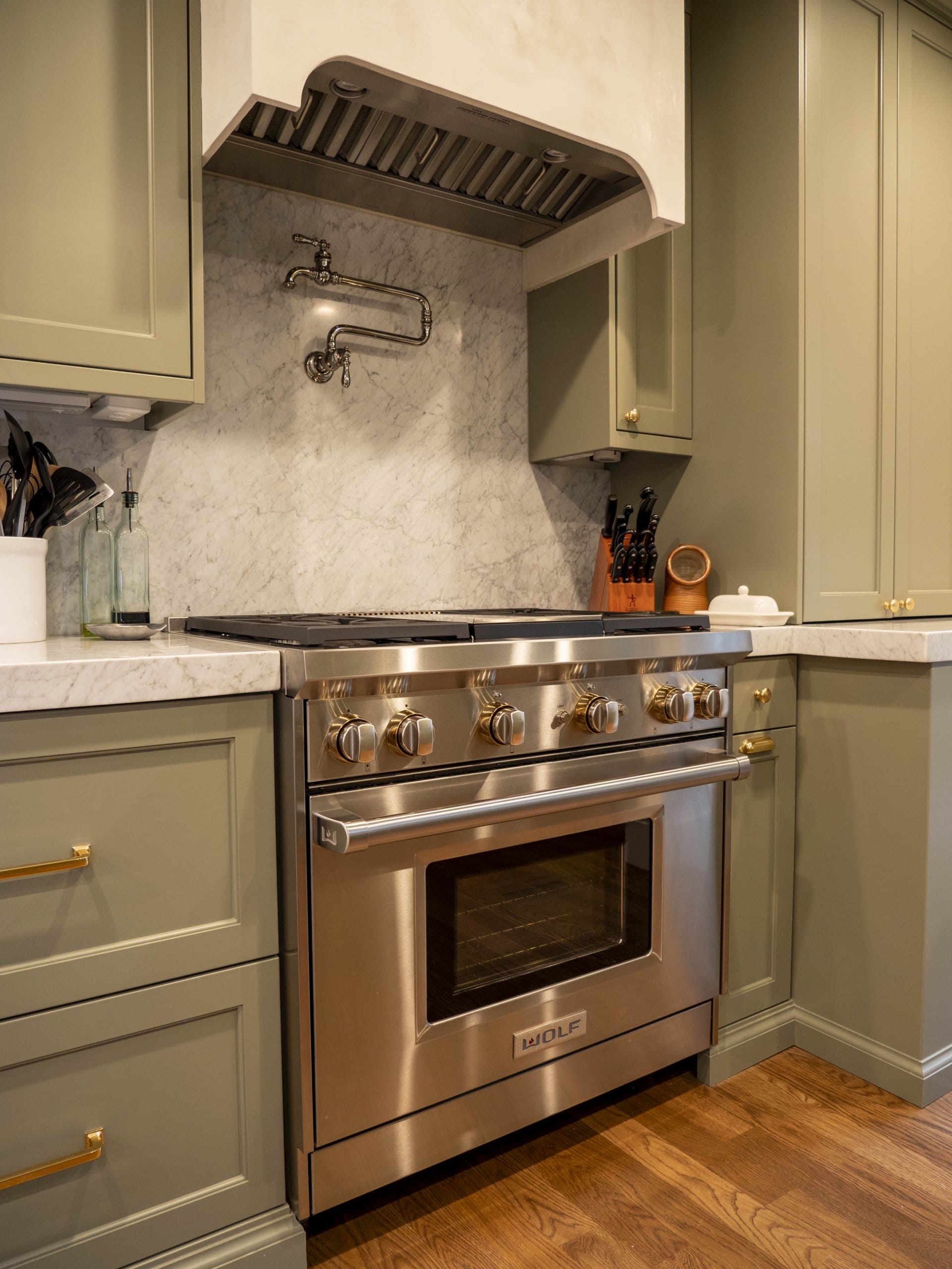 Kitchen range after the remodel with green cabinetry on either side and a pot filler faucet above.