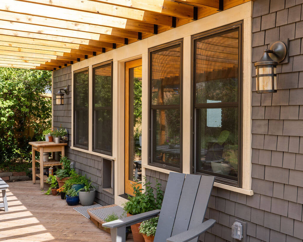 Patio with a pergola above, seating, and lots of plants.