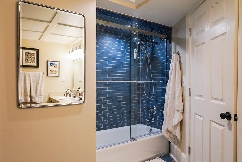 Renovated tub and shower combination with blue tile in the basement bathroom.