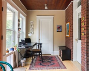 Office area in the addition. A desk is located under the windows on the left, a door is straight ahead, and a bench and door are located to the right.