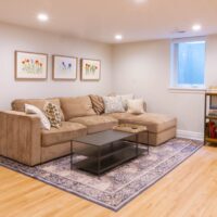 Thumbnail of http://Basement%20family%20room%20with%20couch%20and%20three%20pictures%20hanging%20above,%20a%20bookcase,%20and%20an%20egress%20window.