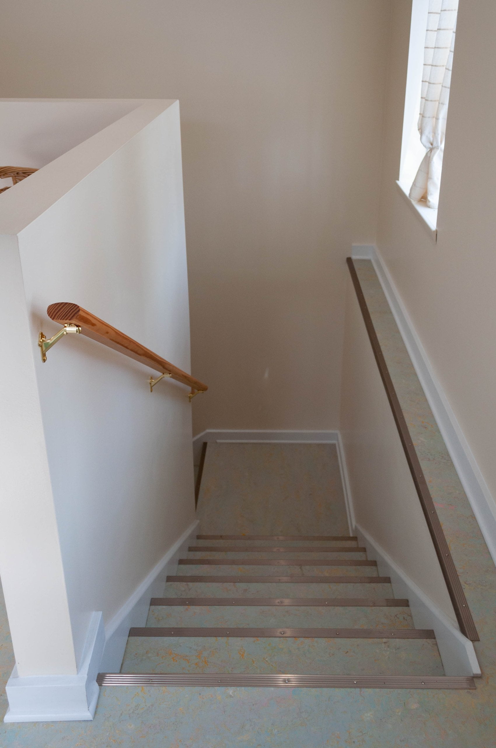 Staircase after the remodel with a landing. On the left, is a partial wall with a railing. On the right, is a window.
