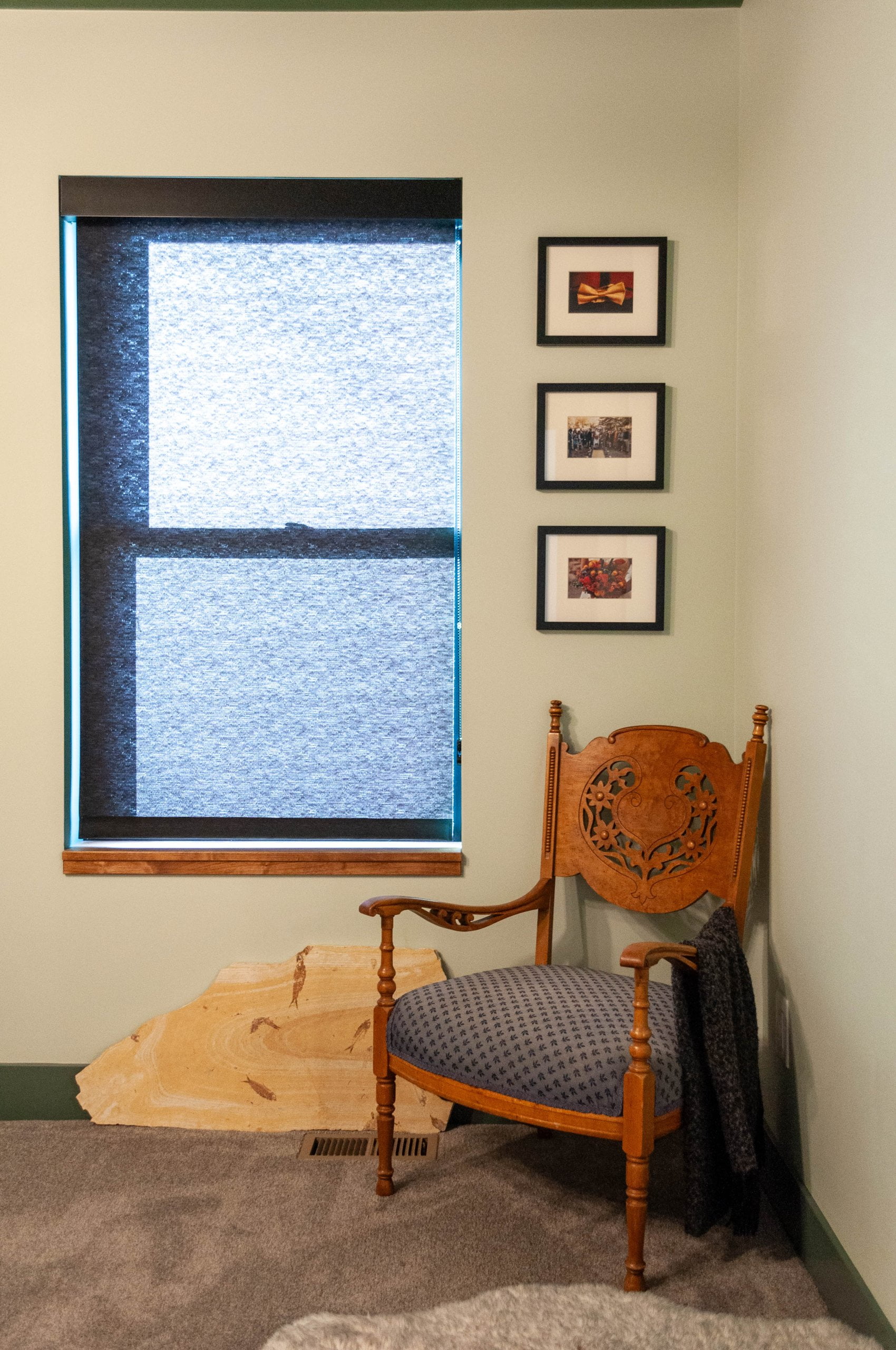 Chair in the corner with three pictures hung on the wall above and a window next to them.