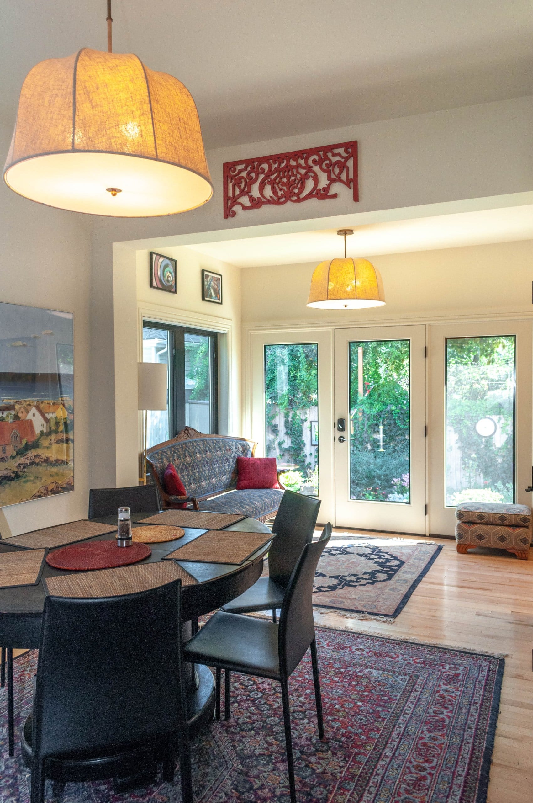 Dining room open to a sitting room with access to the backyard. Both rooms are furnished with pictures on the walls, rugs, and have matching lights hung from the ceilings.